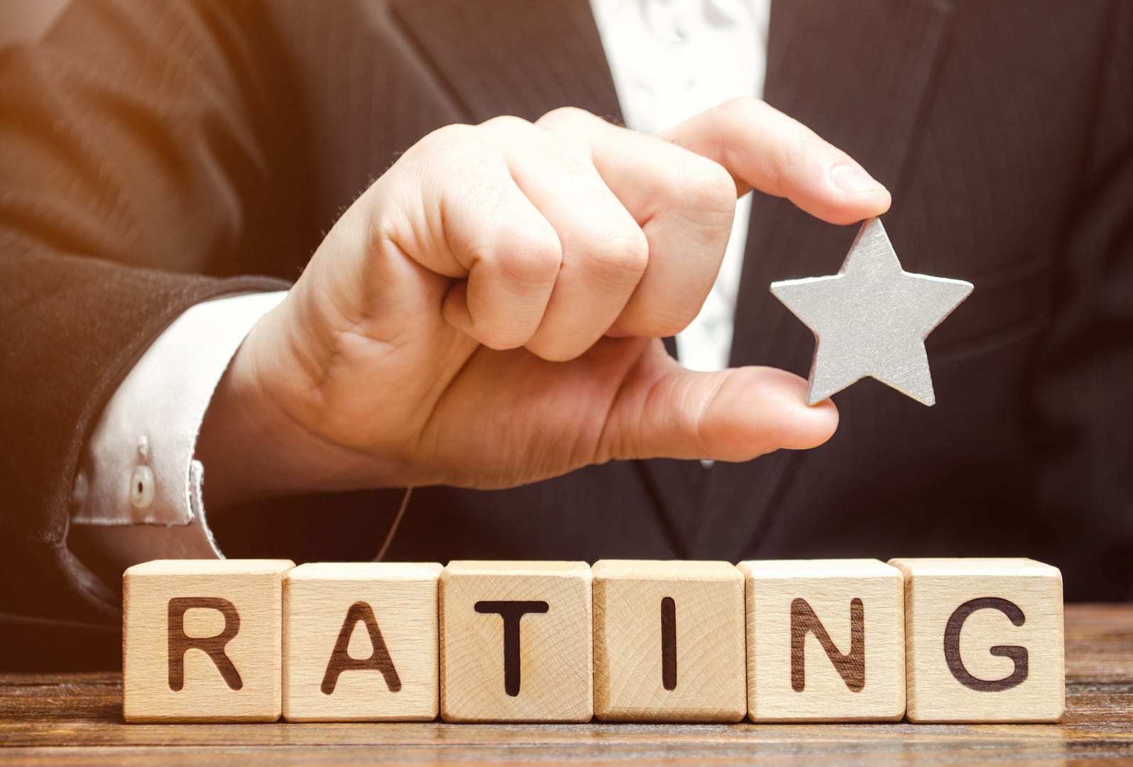 Businessman holds one star above the wooden blocks with the word Rating. Concept of negative feedback. Low quality and service serving. Evaluation of the critic. Hotel or restaurant rating